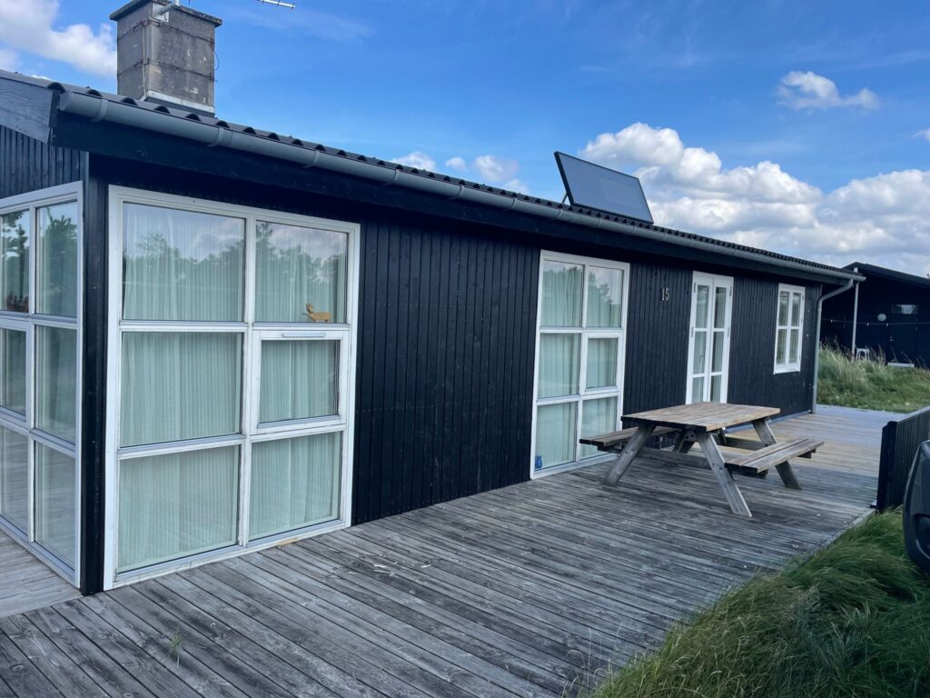 Sort sommerhus med terrasse og picnicbord