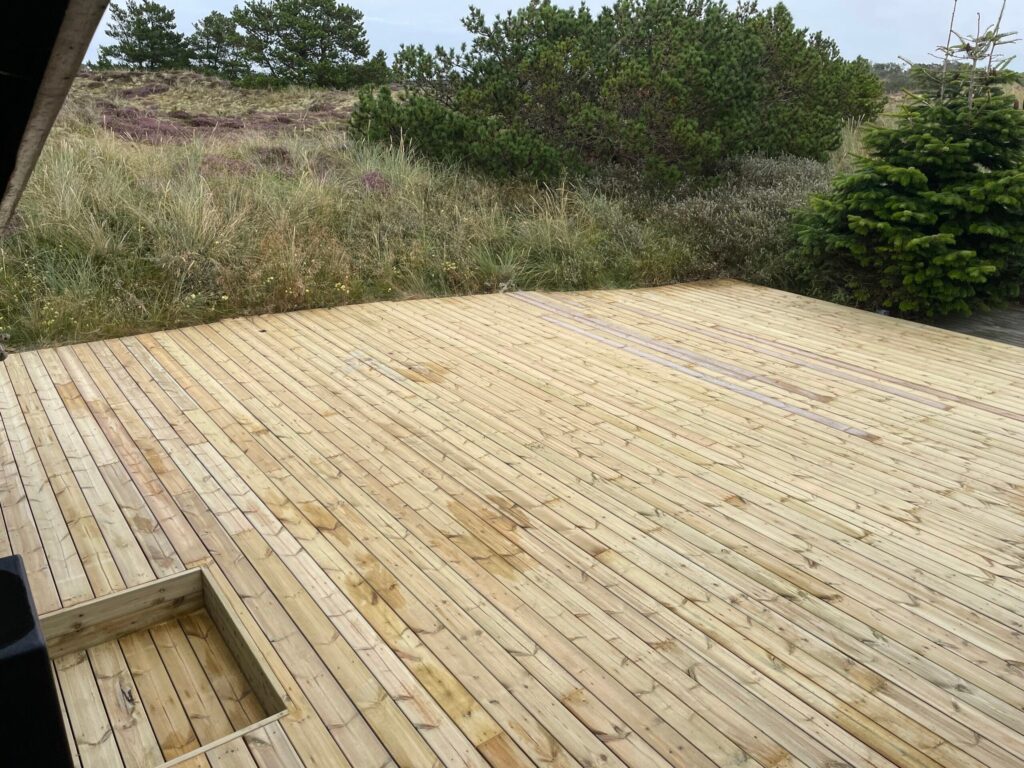 Træterrasse ved siden af grønne buske og græs